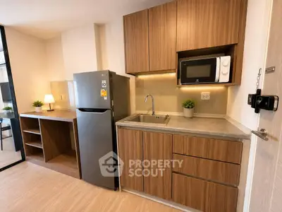 Modern kitchen with sleek wooden cabinets, stainless steel fridge, and microwave in a cozy apartment.