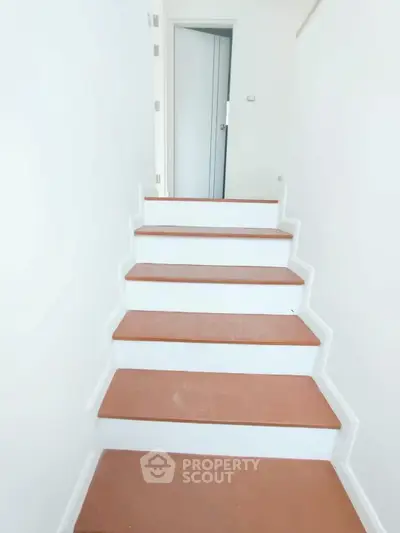Modern staircase with sleek design leading to a closed door in a bright interior space.