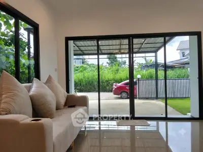 Spacious living room with large windows offering a view of the garden and driveway.