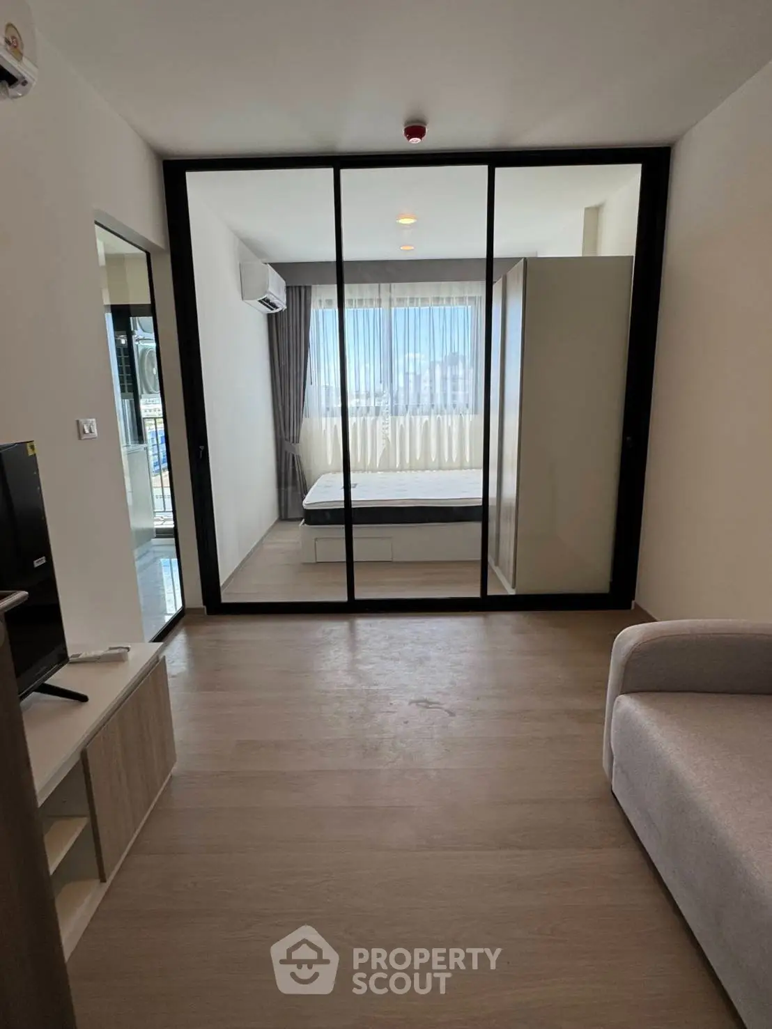 Modern apartment interior with glass partition separating bedroom and living area, featuring sleek design and natural light.