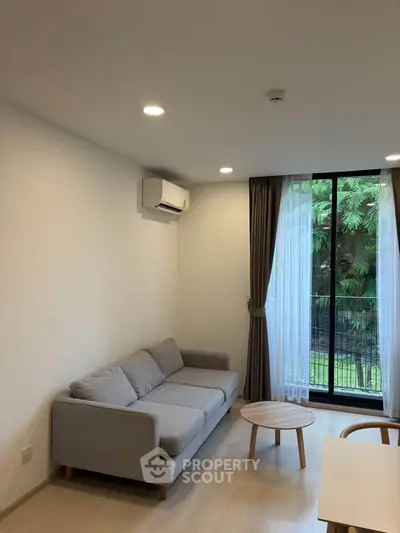 Modern living room with cozy gray sofa, wooden coffee table, and large window with garden view.