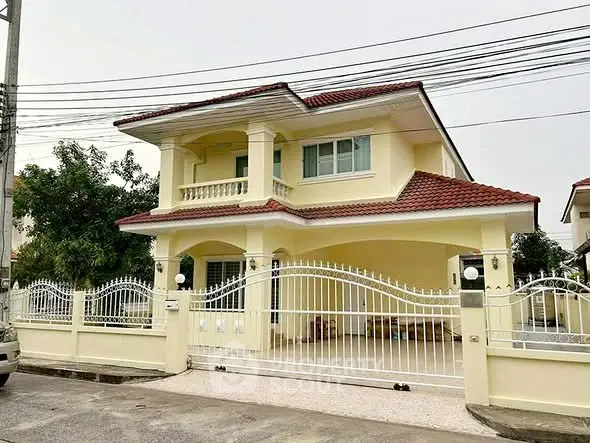 Charming two-story yellow house with red roof and gated entrance in a serene neighborhood.