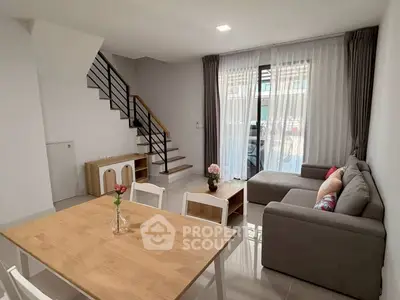 Modern living room with cozy sectional sofa and dining area, featuring large windows and elegant staircase.