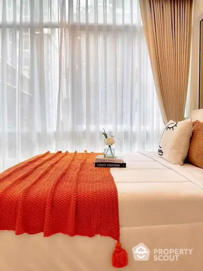 Cozy bedroom with elegant decor and large window, featuring a stylish orange throw blanket.