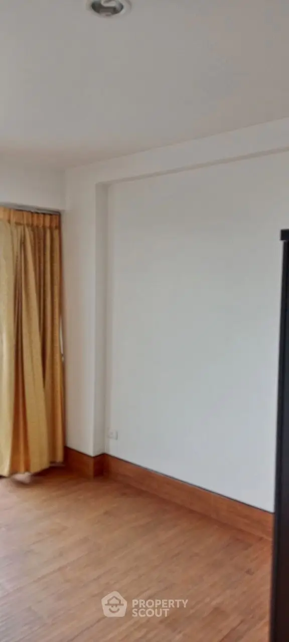 Spacious empty room with wooden flooring and large window with curtains.