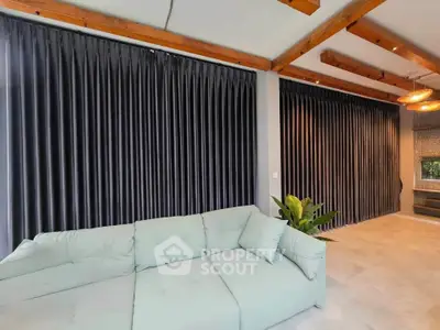 Spacious living room with modern sofa and elegant curtains, featuring exposed wooden beams.