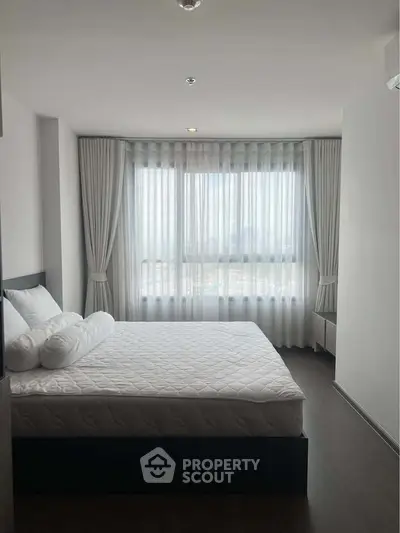 Spacious bedroom with large window and elegant curtains in modern apartment.