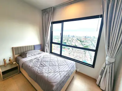 Modern bedroom with stunning city view from large window, featuring cozy bed and elegant curtains.