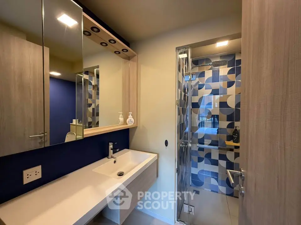 Modern bathroom with stylish blue tile shower and sleek vanity in contemporary home.