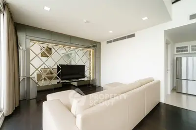 Modern living room with sleek design and large TV, featuring a beige sofa and mirrored wall.