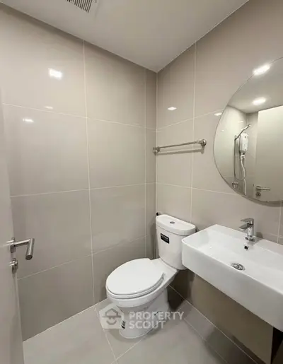 Modern bathroom with sleek fixtures and neutral tiles, featuring a round mirror and compact design.