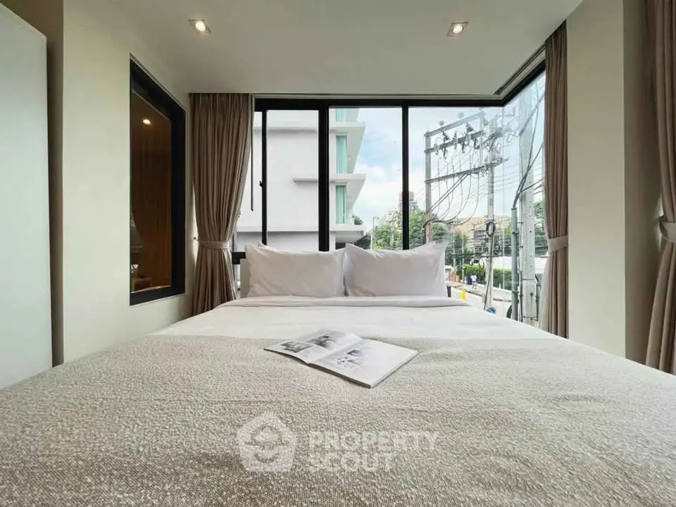 Cozy bedroom with large windows offering a city view, perfect for relaxation and comfort.