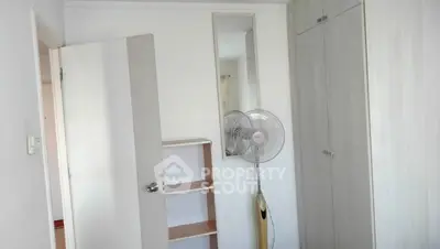 Cozy bedroom with built-in wardrobe and standing fan, perfect for minimalist living.