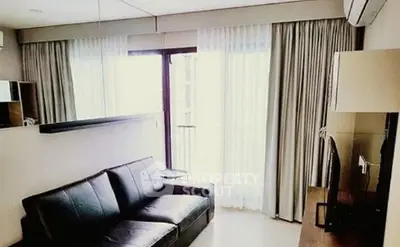 Modern living room with sleek black leather sofa and large window with curtains.