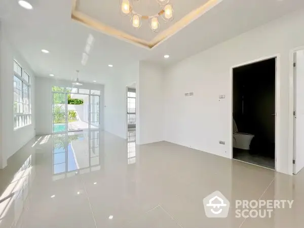 Spacious and bright living room with glossy tiled floors, modern lighting, and large windows allowing ample natural light, perfect for family gatherings.