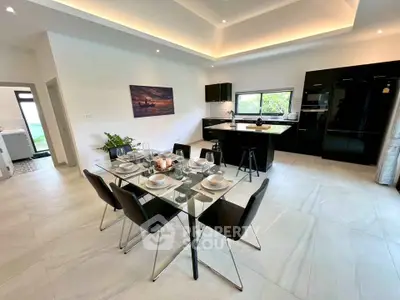 Modern open-plan kitchen and dining area with sleek black cabinetry and elegant glass dining table.