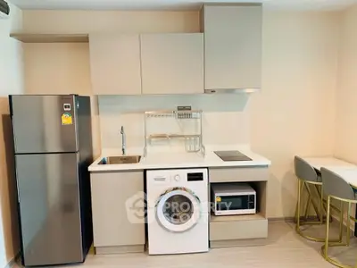 Modern compact kitchen with washing machine, fridge, and microwave in stylish apartment.