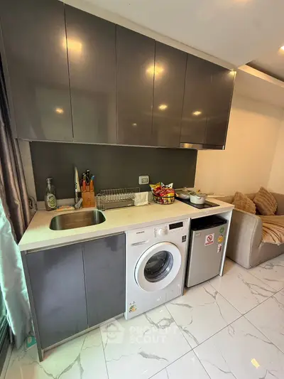 Modern kitchen with sleek cabinets, washing machine, and compact fridge in a cozy apartment.