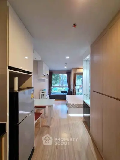 Modern open-plan living space with kitchen and cozy seating area, featuring large windows and stylish decor.