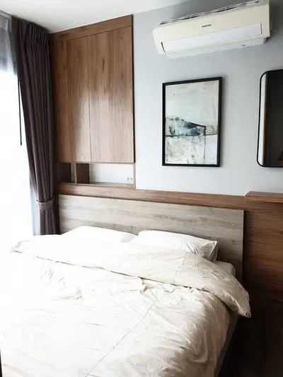 Cozy bedroom with modern decor and natural light, featuring a stylish wooden headboard and wall-mounted air conditioner.