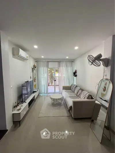 Modern living room with sleek furniture and natural light, featuring a cozy sofa and wall-mounted TV.