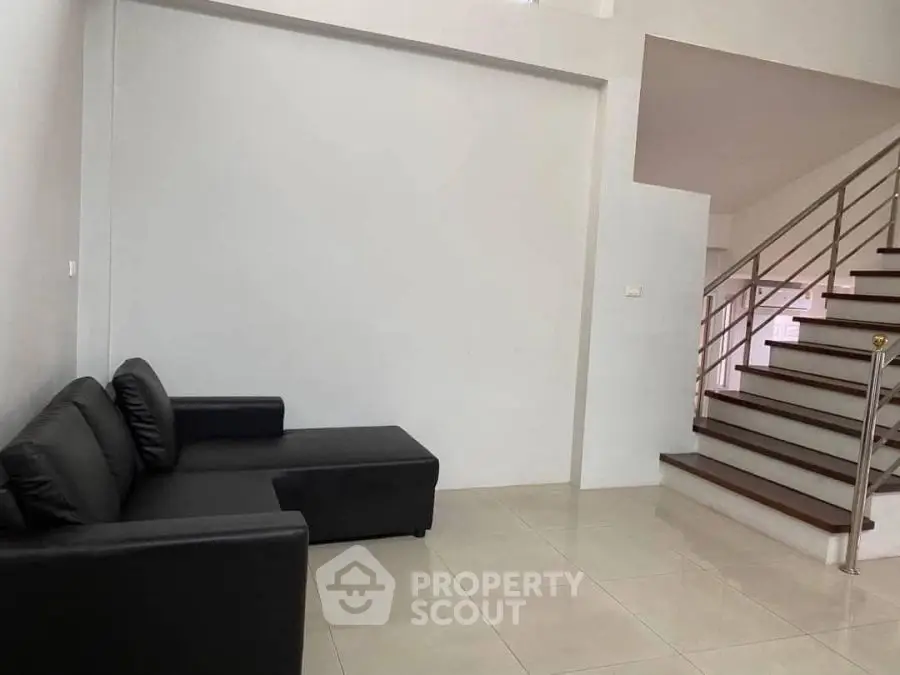 Modern minimalist living room with sleek black sofa and stylish staircase