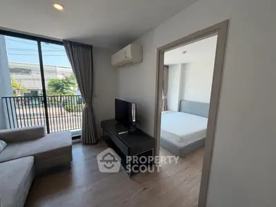 Modern apartment living room with balcony and bedroom view, featuring sleek furniture and natural light.