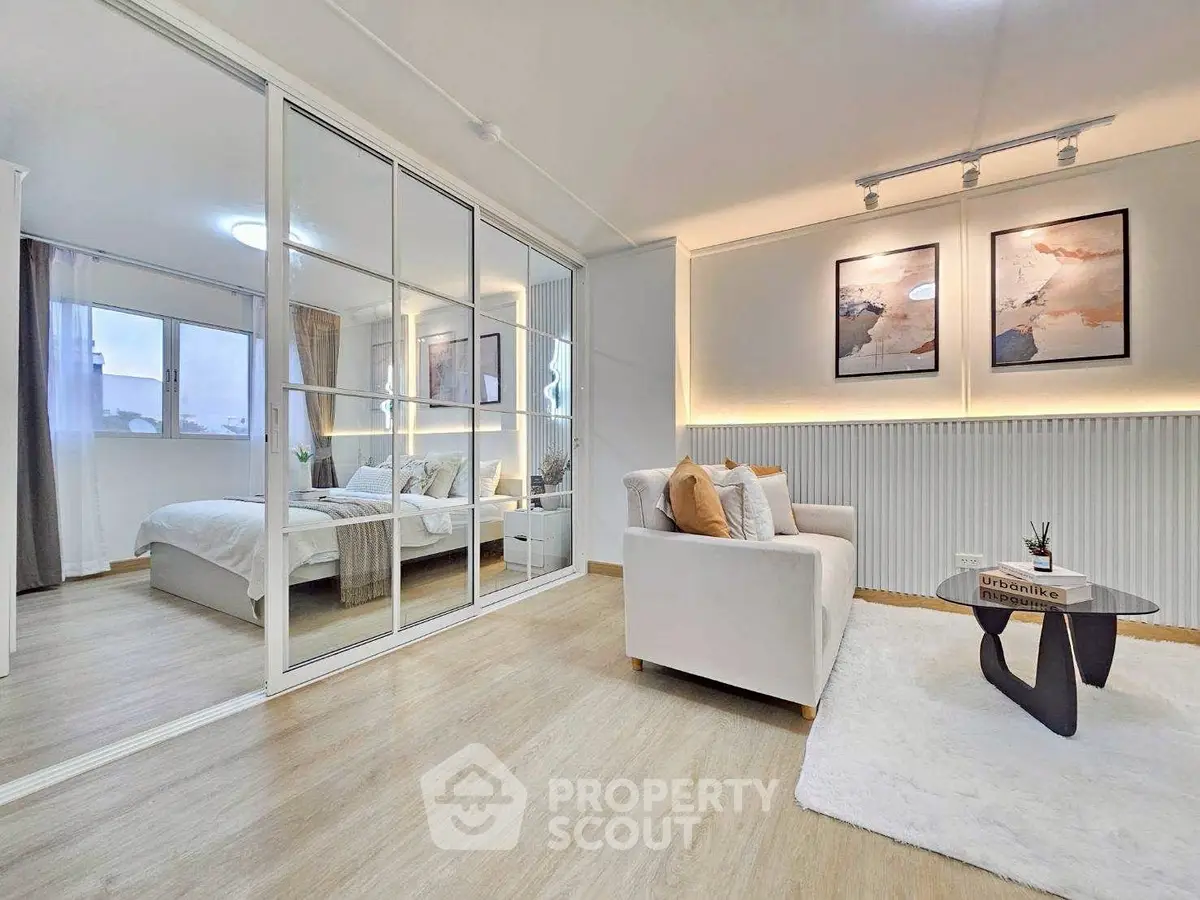Modern open-plan living room with stylish decor and mirrored sliding doors leading to a cozy bedroom.
