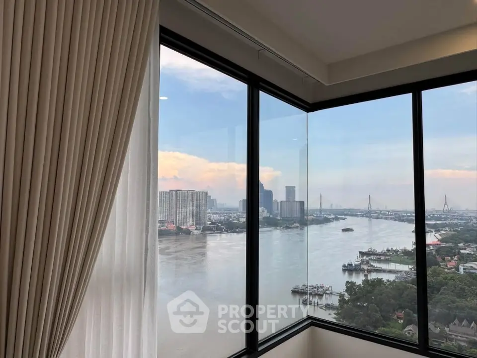 Stunning river view from high-rise apartment with floor-to-ceiling windows and elegant curtains.