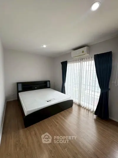 Spacious bedroom with large window and modern furnishings in a well-lit apartment.