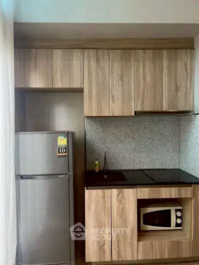 Modern compact kitchen with wood cabinets, fridge, and microwave in stylish apartment.