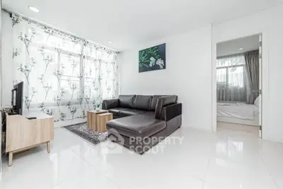 Modern living room with sleek leather sofa and floral curtains, adjacent to a cozy bedroom.