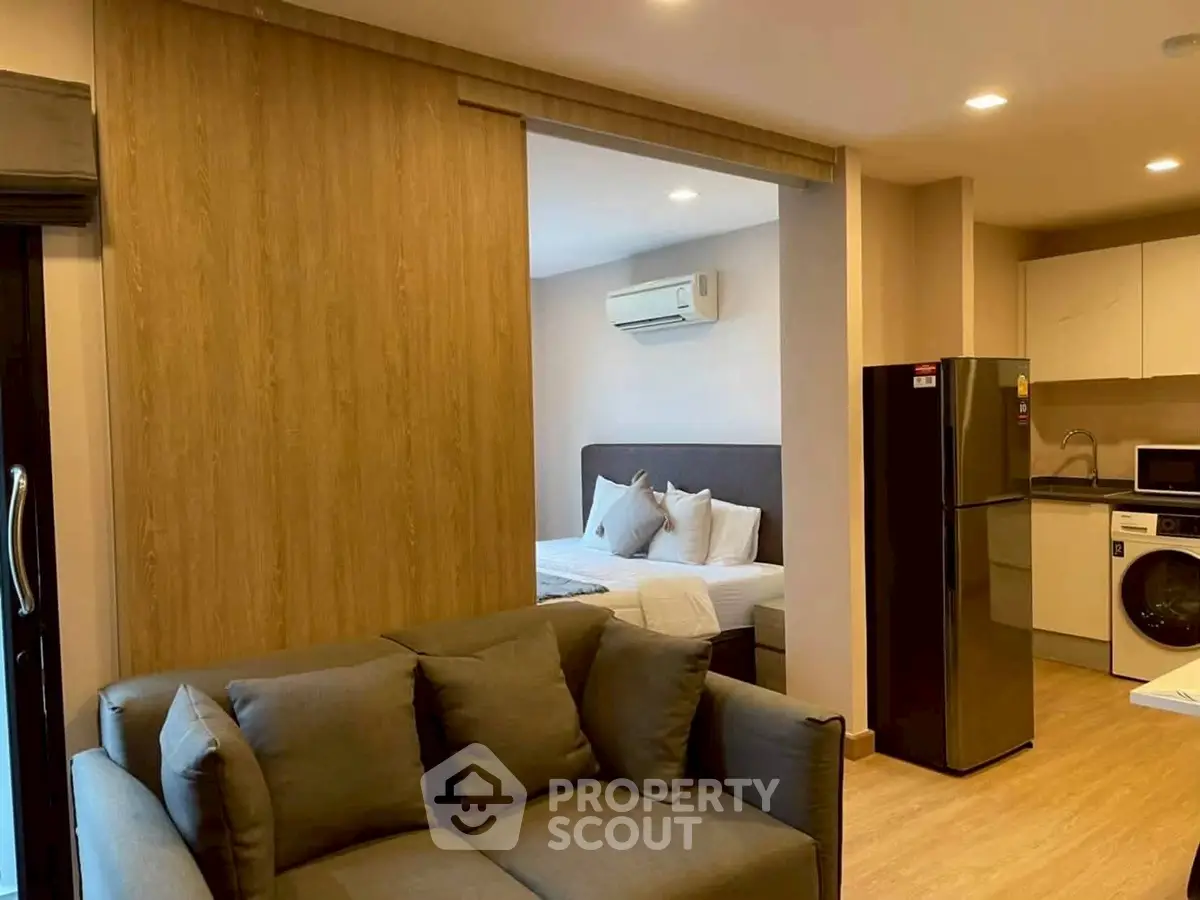 Modern open-plan living room with kitchen and bedroom, featuring sleek appliances and cozy furnishings.