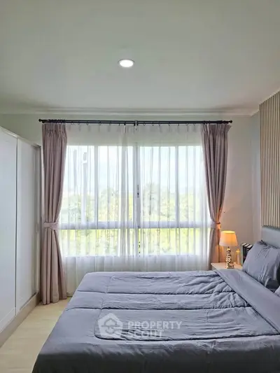 Bright and cozy bedroom with large window and elegant curtains, perfect for relaxation.