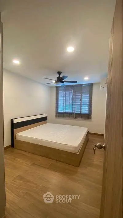 Cozy bedroom with wooden flooring and ceiling fan, featuring a large window for natural light.