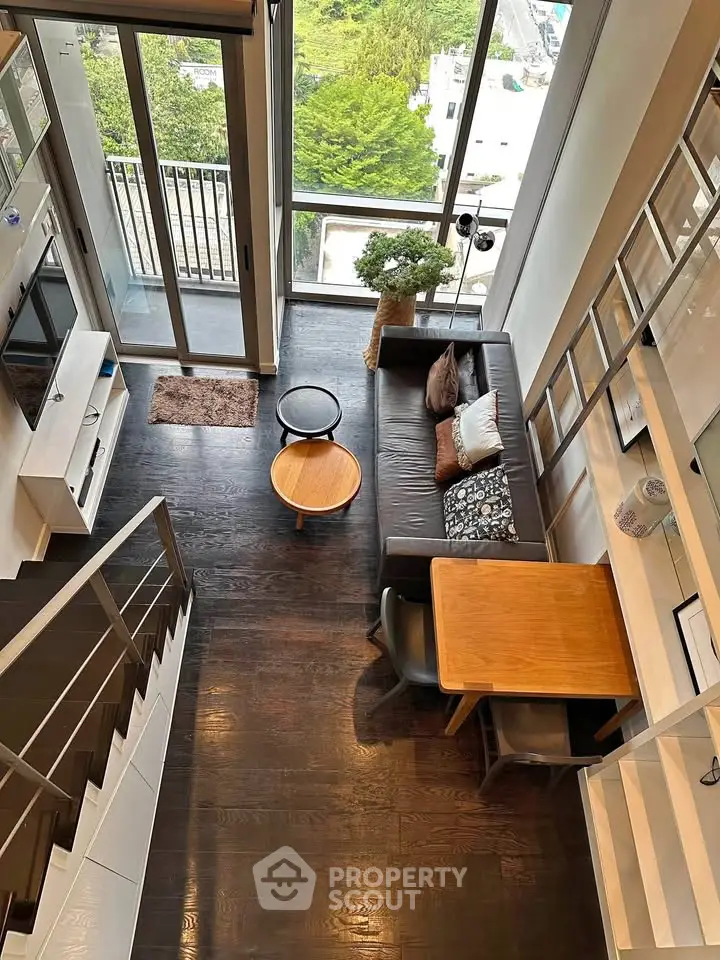 Modern loft-style living room with high ceilings and balcony view, featuring sleek furniture and dark wood flooring.