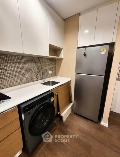 Modern kitchen with sleek cabinets, stainless steel fridge, and washing machine in compact layout.