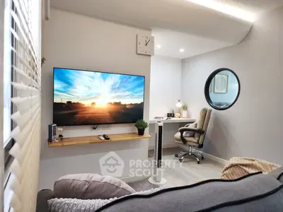 Modern living room with large TV and cozy workspace, featuring stylish decor and natural lighting.