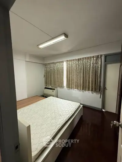 Cozy bedroom with natural light and wooden flooring, featuring a comfortable bed and air conditioning.