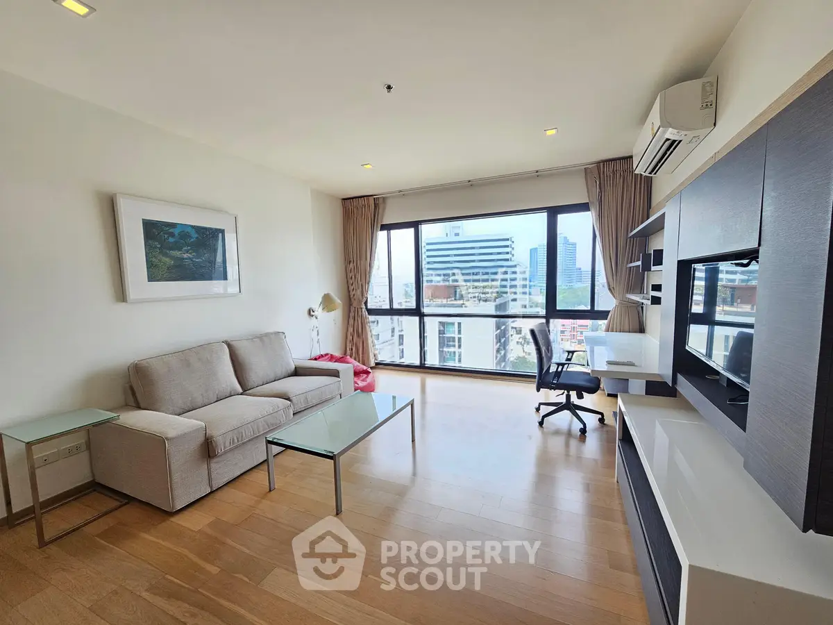 Spacious modern living room with city view, featuring sleek furniture and large windows.