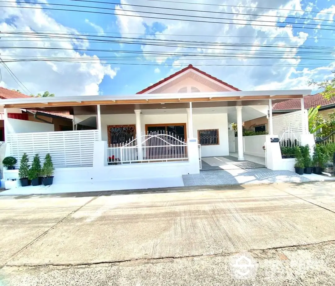 Charming single-story home with a spacious covered porch, elegant white fencing, and a red-tiled roof, nestled in a serene neighborhood.