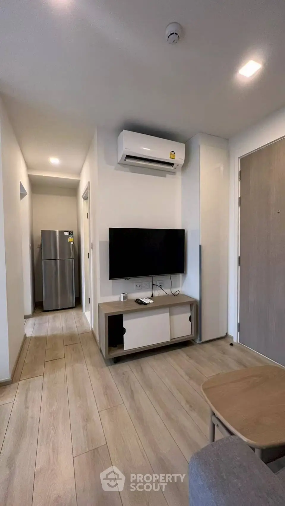 Modern living room with sleek design, featuring a wall-mounted TV and air conditioning, leading to a kitchen area.