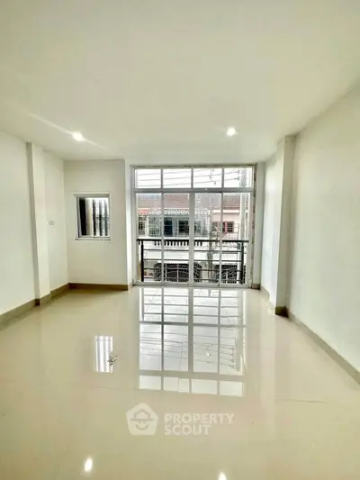 Spacious living room with large windows and glossy floors, offering abundant natural light.