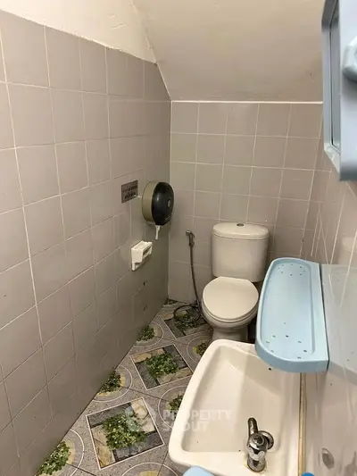 Compact bathroom with toilet, sink, and tiled walls in a cozy real estate property.