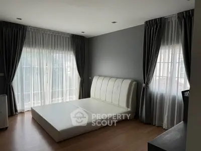 Spacious bedroom with large windows and elegant curtains, featuring a modern bed frame.