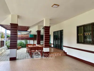 Spacious covered patio with elegant wooden furniture and tiled flooring, perfect for outdoor relaxation.
