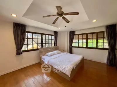 Spacious bedroom with wooden flooring and ceiling fan, featuring large windows for natural light.