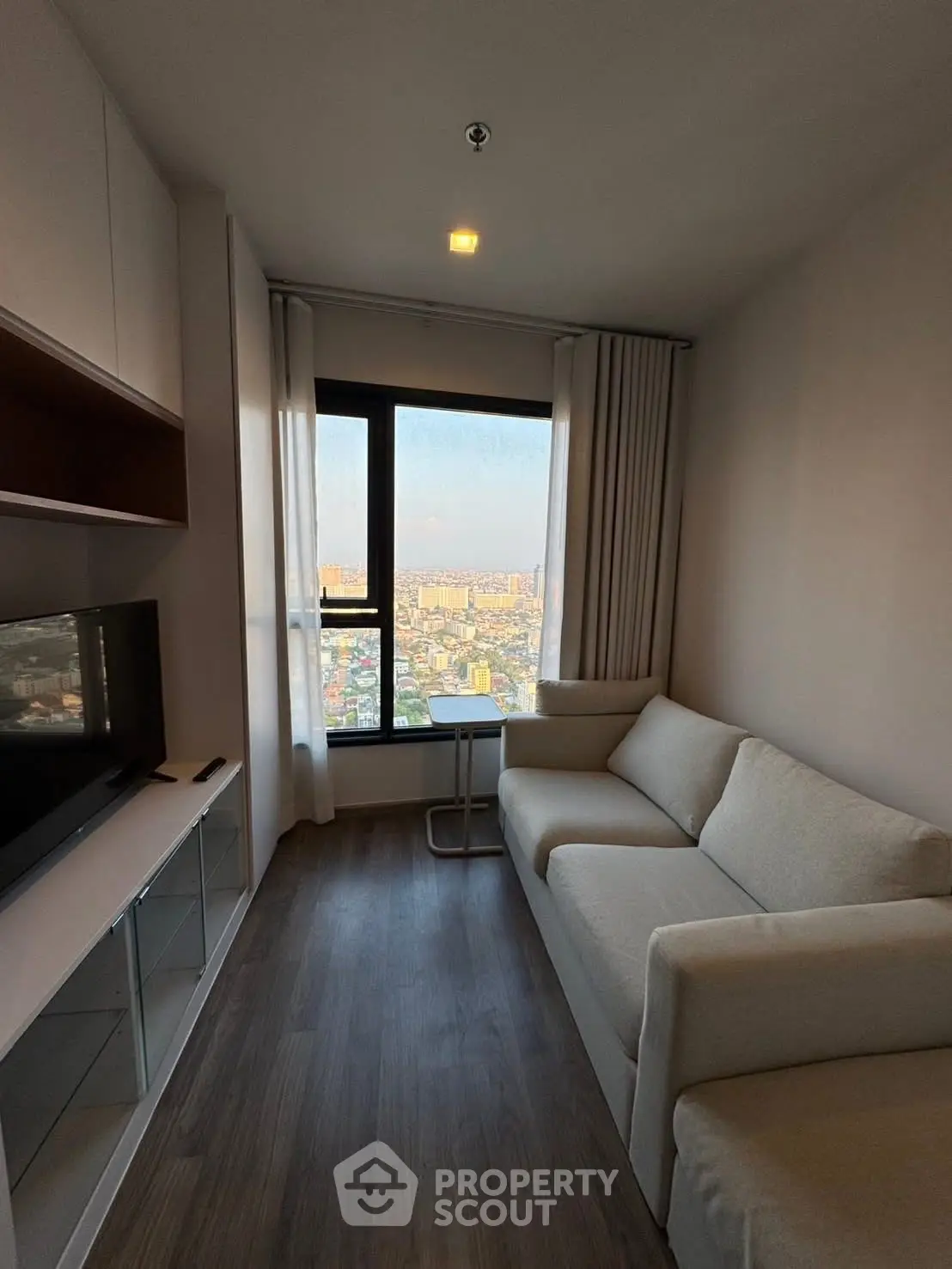 Modern living room with city view, featuring sleek furniture and large window for natural light.