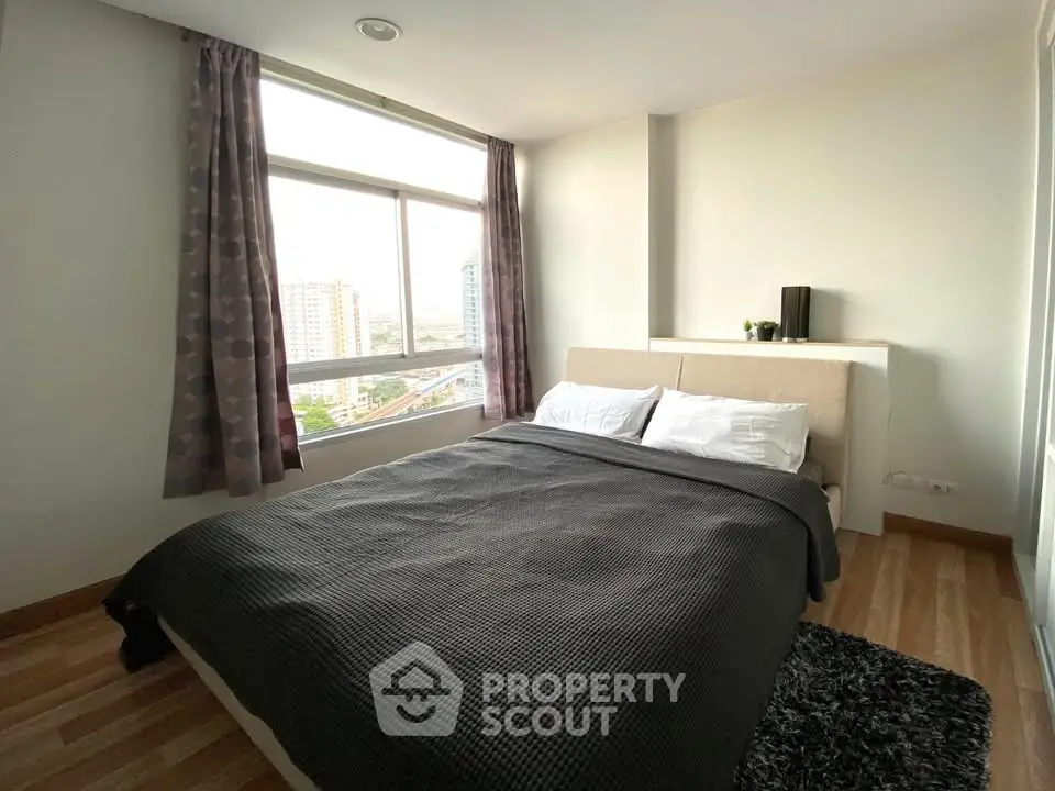 Spacious bedroom with large window offering stunning city views, featuring a cozy bed and modern decor.