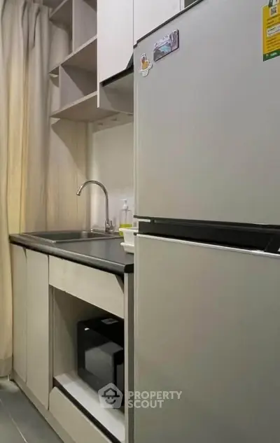 Compact modern kitchen with fridge, microwave, and sleek cabinetry in cozy apartment.